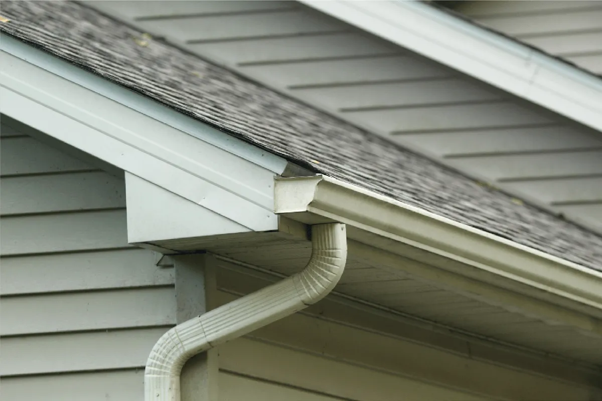 Professional gutter technician clearing debris from a residential roofline